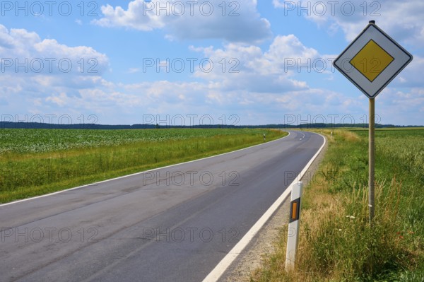 Empty, winding road with traffic sign and wide sky with clouds, Hausen, Würzburg district,