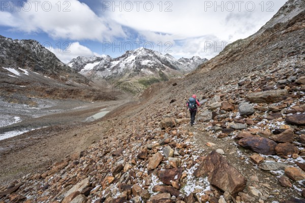 Mountaineer on hiking trail in steep rocky mountain landscape with fresh snow in summer, mountain