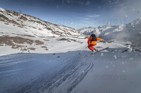 An athlete male skier jumps from a snow-covered slope against the backdrop of a mountain landscape