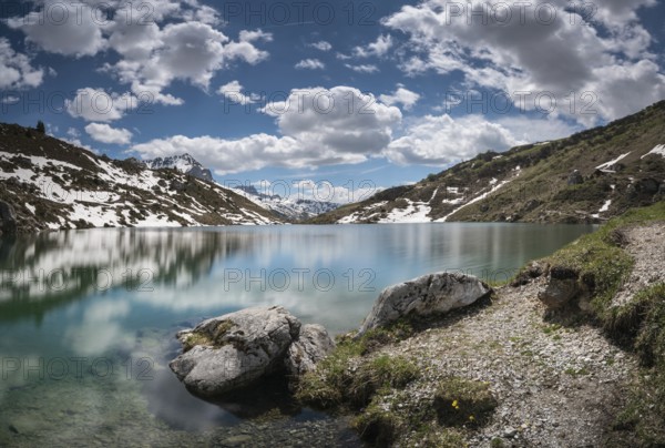 gorgeous mountain lake in the Alps with reflections and snow remnants under a blue sky with white