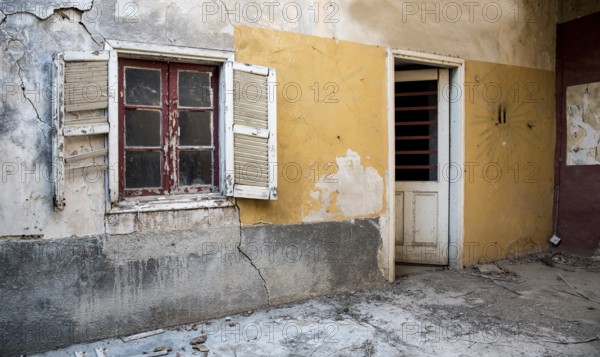 Backyard of a deserted abandoned house with a broken closed window and door and with yellow cracked