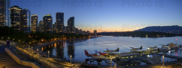 Harbour view at sunset with seaplanes and illuminated skyline in the background, Vancouver, British