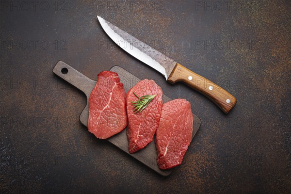 Three raw uncooked meat beef top sirloin steaks on wooden cutting board with rosemary on wooden