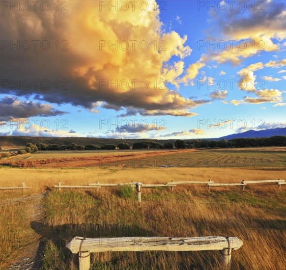 The huge cloud lit yellow-orange rays of sunset. Cozy wooden bench by the side of the road in