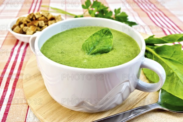 Green soup puree in a bowl with green leaf spinach, spoon on the board, croutons, parsley on a
