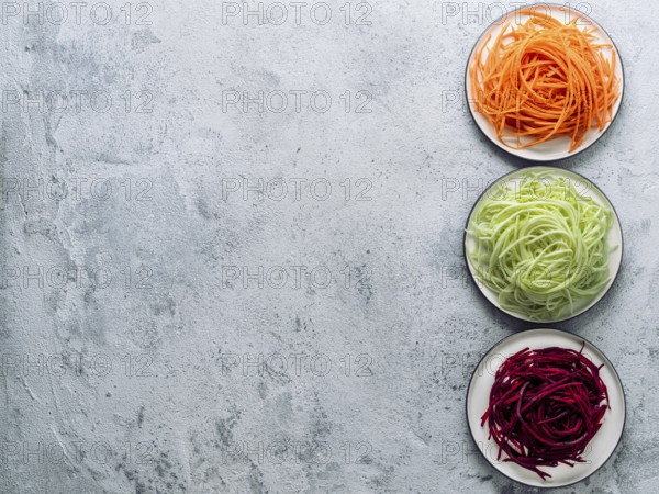 Vegetable noodles - zucchini, carrot, and beetroot noodles on plate over gray cement background.