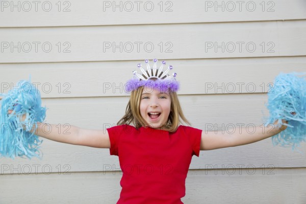 Blond kid girl playing like cheerleading pom poms with princess crown