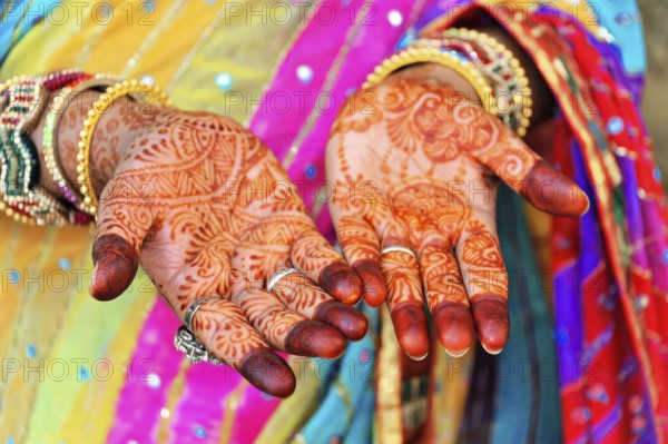 Close-up of painted hands with elaborate mehndi designs, accompanied by colourful robes, Rajasthan,