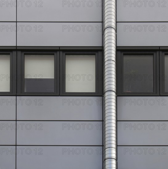Grey cladding panels on an industrial building with a row of back window frames and a silver pipe