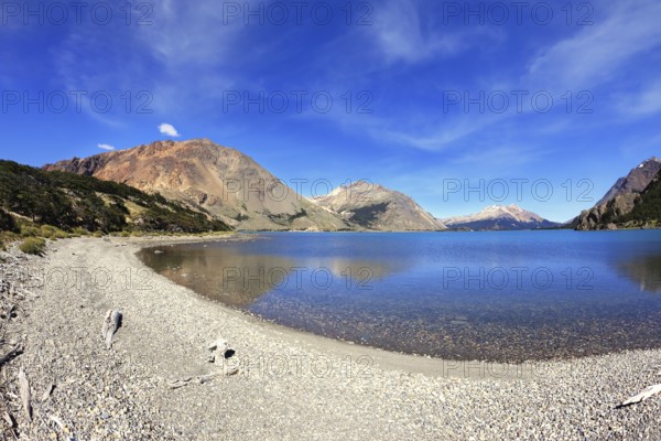 Oval blue lake surrounded by mountains. Mountains reflected in the mirrored water. Picture taken