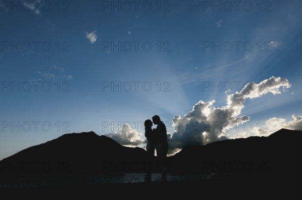 Silhouettes of a man and a woman who hug and kiss at sunset on the seashore against the background