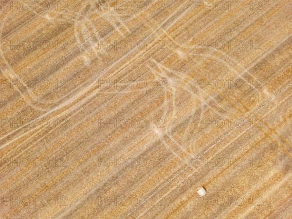 Striking tracks and patterns from a tractor on a dry agricultural field with straw bales, aerial