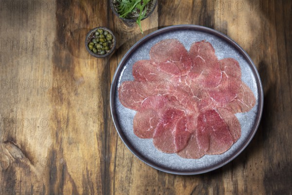 Food, Marbled beef for carpaccio with ingredients arugula and capers on gray plate, wooden