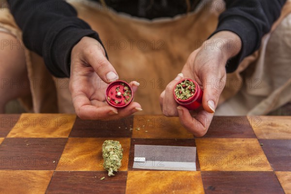 Selective focus closeup of person's hands holding a red weed filled grinder shot from above.