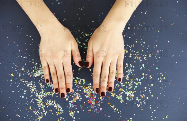Top view of crop anonymous female with bright manicure over dark blurred background with colorful