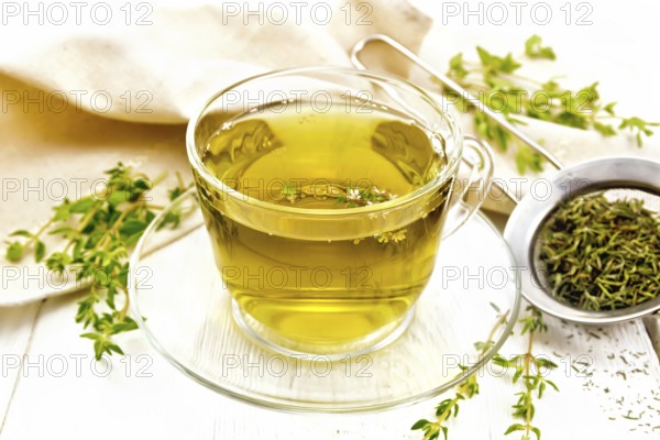 Herbal tea in a glass cup of thyme, a metal strainer with dry leaves, a linen napkin on the