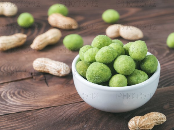 Peanut snack for beer, wine, party bar. Salted peanuts in green vasabi glaze on brown wooden table.