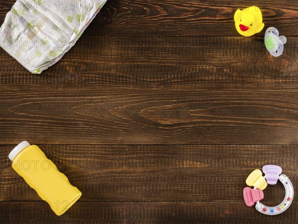 Disposable diaper, teether, dummy, baby powder and rubber duckling on dark wooden background with