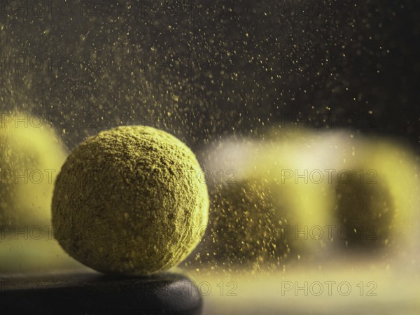 Homemade truffles candy with matcha tea powder in green tea dust cloud over dark background. Copy