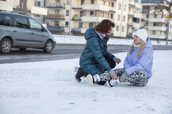 A woman who has fainted is sitting on the sidewalk. The sidewalk is covered with snow. Next to the