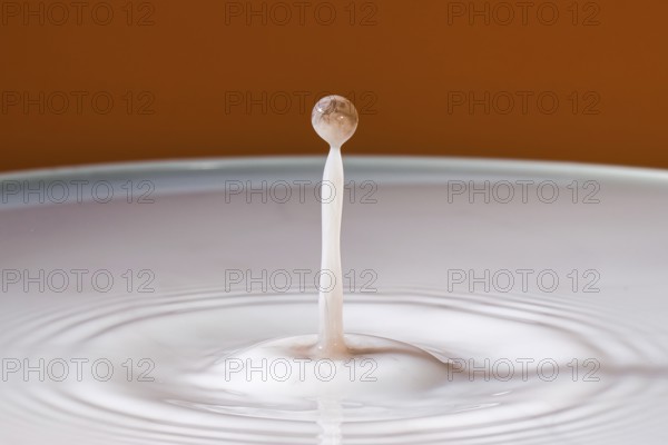 Single dripping water jet hits smooth surface in front of orange background, water droplets,