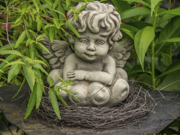 Angel statue in a nest of twigs, surrounded by green leaves in the garden, borken, münsterland,