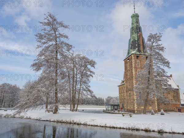 Castle with high tower in winter. Snow-covered trees and a frozen lake in the foreground, Raesfeld,