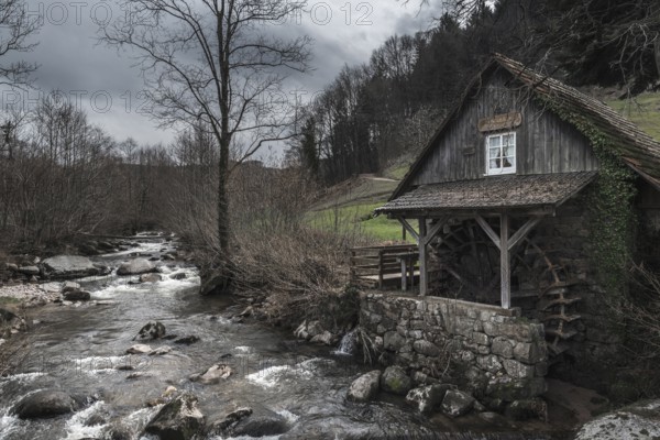 Vintage landscape with an old, abandoned water mill on an alpine river shore, on a cloudy day of