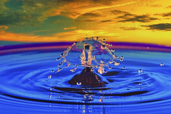 A drop of water in the middle of a lake with a colourful sunset in the background, highspeed