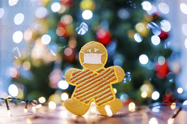 Gingerbread man in a protective icing mask on the table in the light of multi-colored lights on the