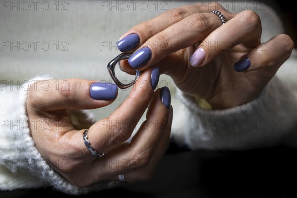 A woman's manicured hands with blue and pink nails hold a pair of eyeglasses, featuring elegant