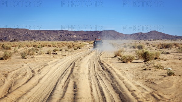 An off-road vehicle drives on a dusty sandy track in an arid desert, With the off-road vehicle