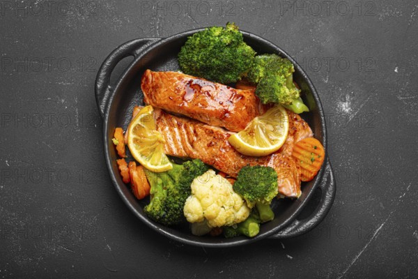 Healthy baked fish salmon steaks, broccoli, cauliflower, carrot in cast iron casserole bowl black