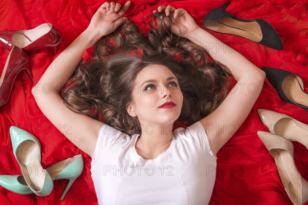 Beautiful woman with blue eyes and red lips, lays on a red fabric, smiling and surrounded by many