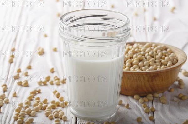 Non-dairy alternative Soy milk or yogurt in mason jar on white wooden table with soybeans in bowl