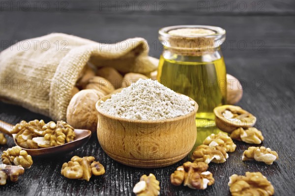 Walnut flour in bowl, nuts on a table, in a spoon and in a bag, oil in glass jar on wooden board