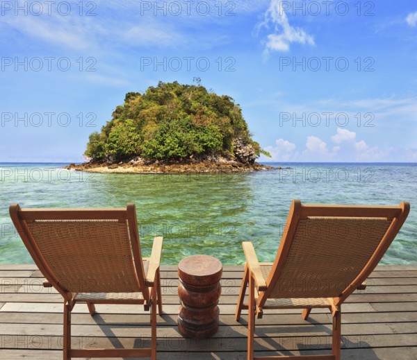 The charming landscape. A green island in a sea bay with emerald water. Two wooden chairs - on a