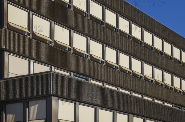 Sunlight illuminating rows of windows and awnings on a modern building facade, creating a