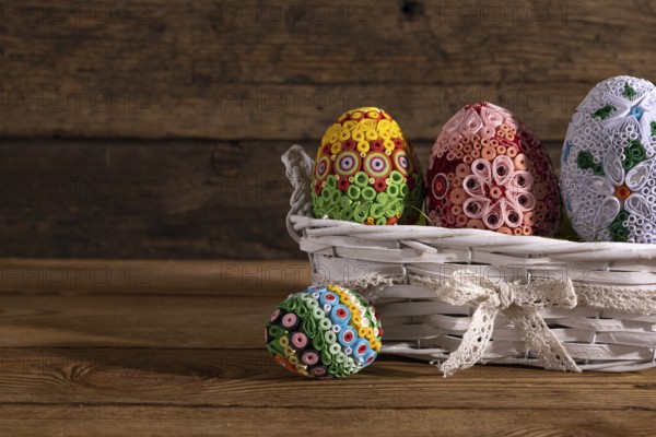On a background of brown boards set a woven basket with colorful Easter eggs. Easter composition as