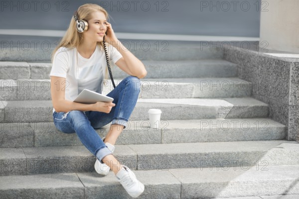 Happy young woman with vintage headphones and a cup of coffee to go, surfing the internet on a