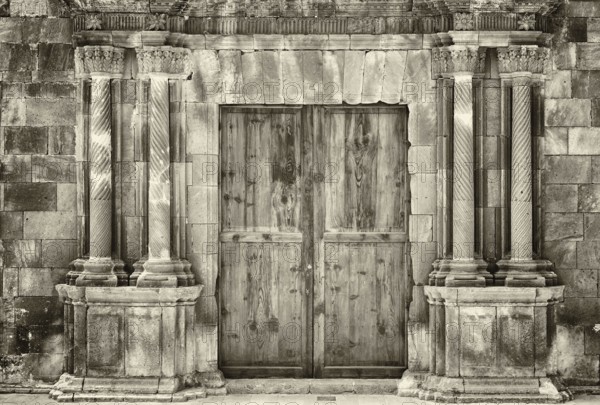 Monochrome sepia ancient wooden double doors in an old stone building with crumbling ornate columns