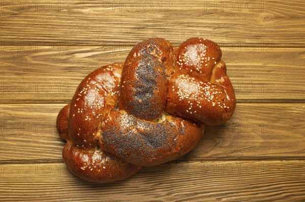 Freshly baked Challah bread covered with poppy and sesame seeds, top view on rustic wooden