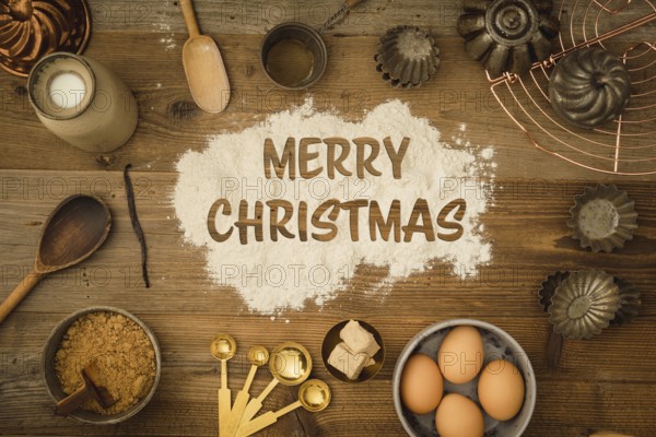 Collection of ingredients and utensils for baking on a dark wooden table with the words Merry