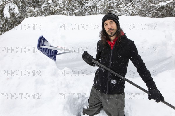 Satisfied and happy man smiling as he standing between snow piles holding a shovel to removing