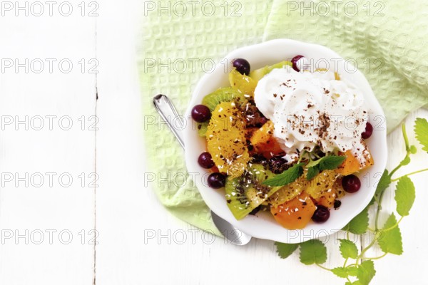 Fruit salad with orange, kiwi, cranberries and baked pumpkin, whipped cream, sprinkled with