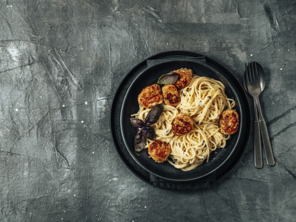 Zucchini Parmesan Meatballs with Pasta Carbonara in black craft plate over gray background. Close