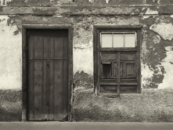 Monochrome image of the front of an old abandoned house with shuttered windows and locked wooden