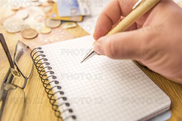 Close-up image with a blank math notebook and a man's hand holding a pen. In the background there