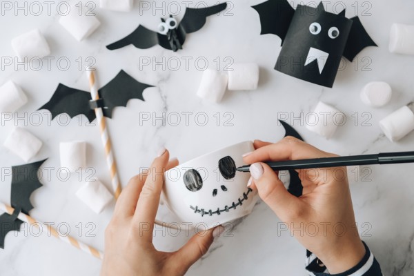 Female hands paint on white cup scary jacks face DIY for kids Halloween home activities Holiday art