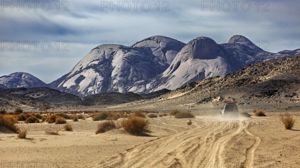 A vehicle moves along a dusty track through a vast desert landscape, travelling through the Sahara